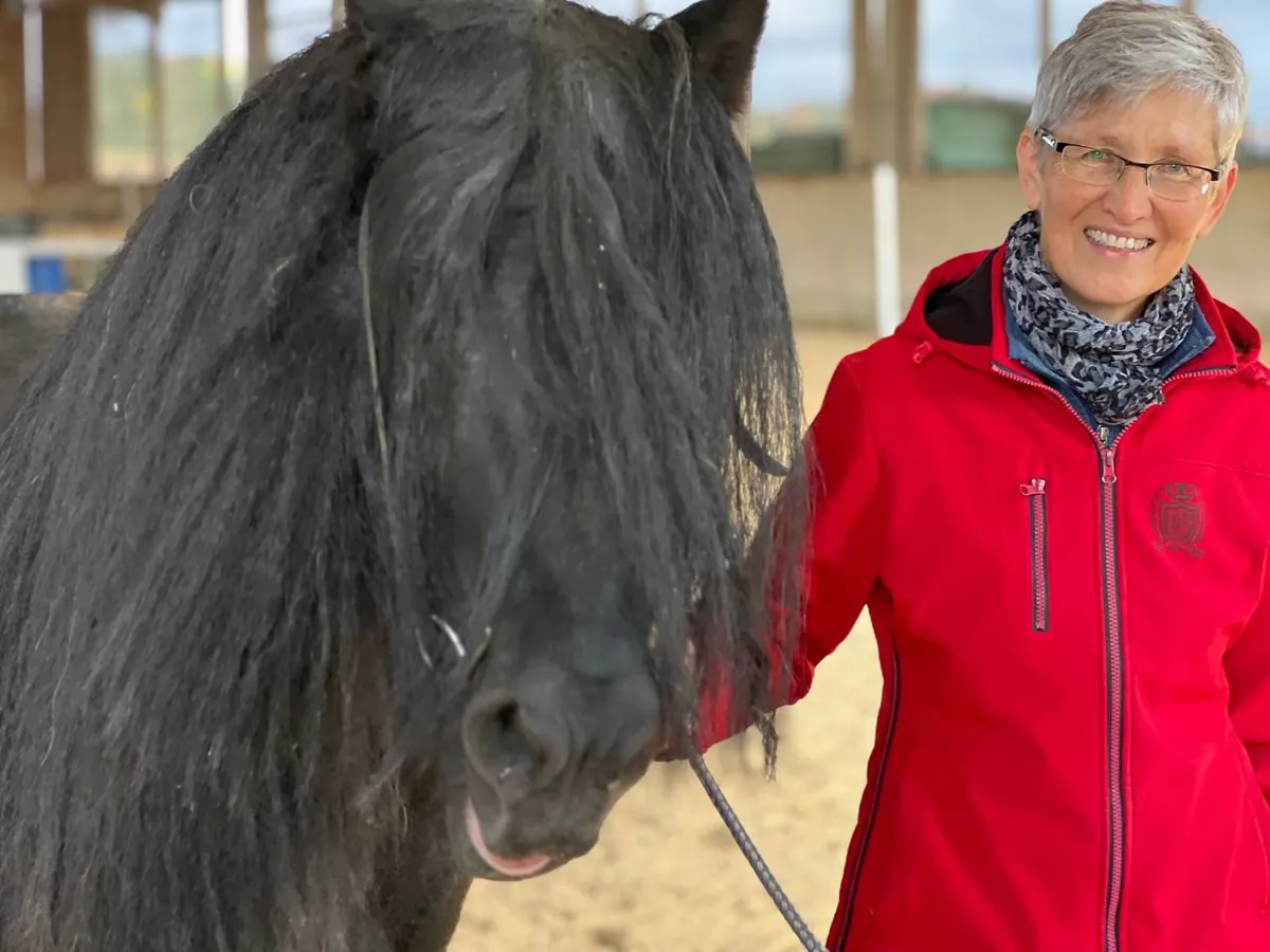 Gudrun Köppel in roter Jacke mit einem schwarzen Pferd in der Reithalle