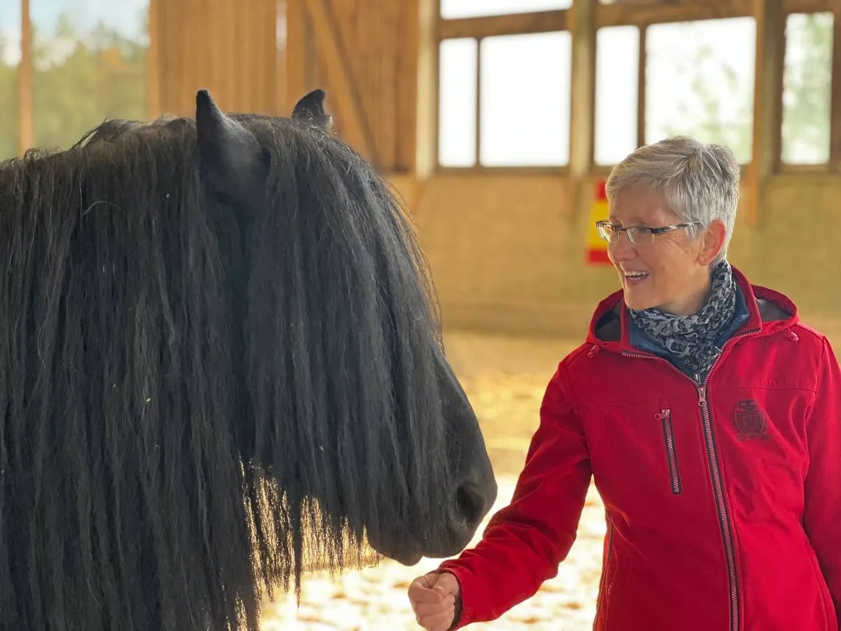 Gudrun Köppel in roter Jacke mit einem schwarzen Pferd in der Reithalle